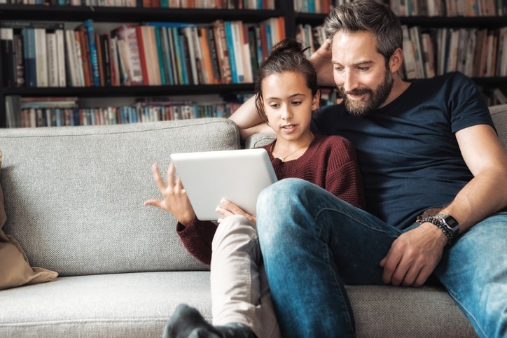 happy father and daughter at sofa looking at digital tablet